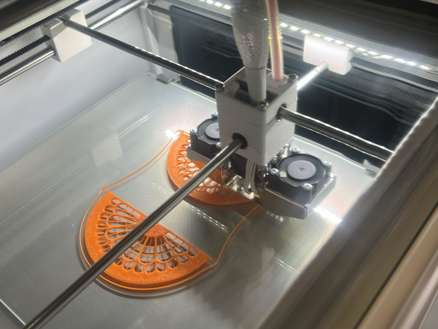 A 3D printer creates orange replicas of model pieces created by architecture students.