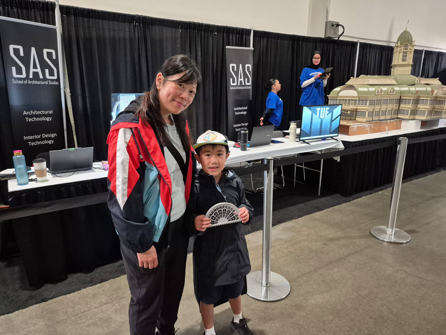 A young future architect and his mom visit and chat with George Brown students restoring the Crystal Palace model at the CNE.
