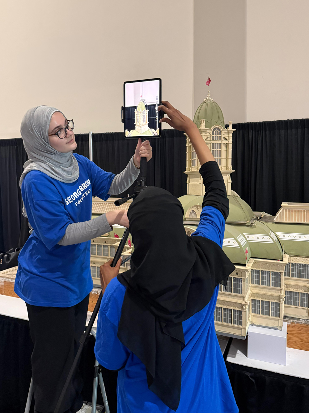 Two students use a device to do a 3D scan of the Crystal Palace model at the Canadian National Exhibition.