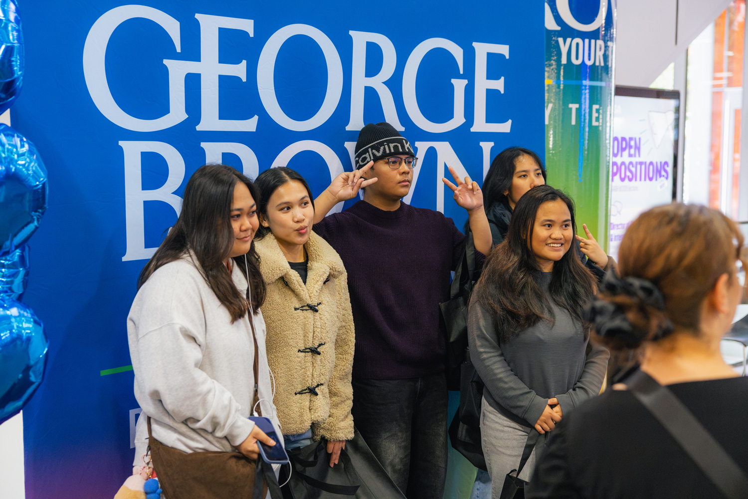 A group of visiting students take a selfie at the Photo Booth against a George Brown backdrop.
