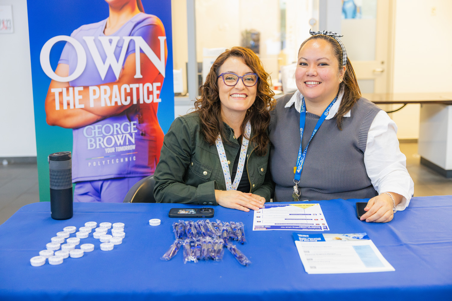 Two health sciences staff are seated at a table sharing information with visiting high school students at the CIP event.