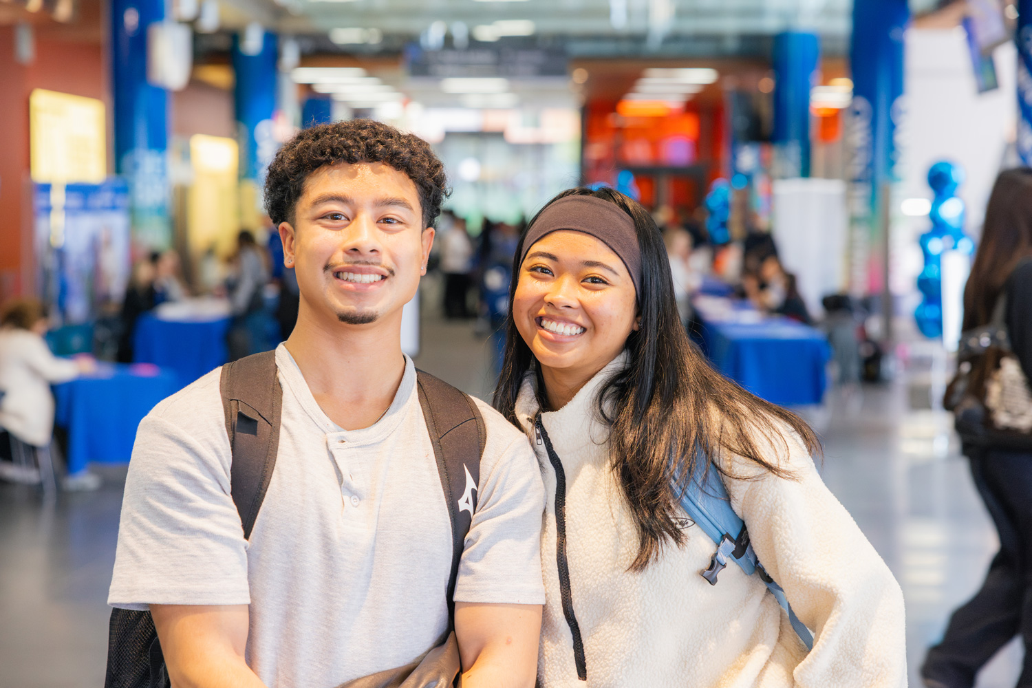 Two students visiting the College Information Program event smile with tables and other visitors in the background.