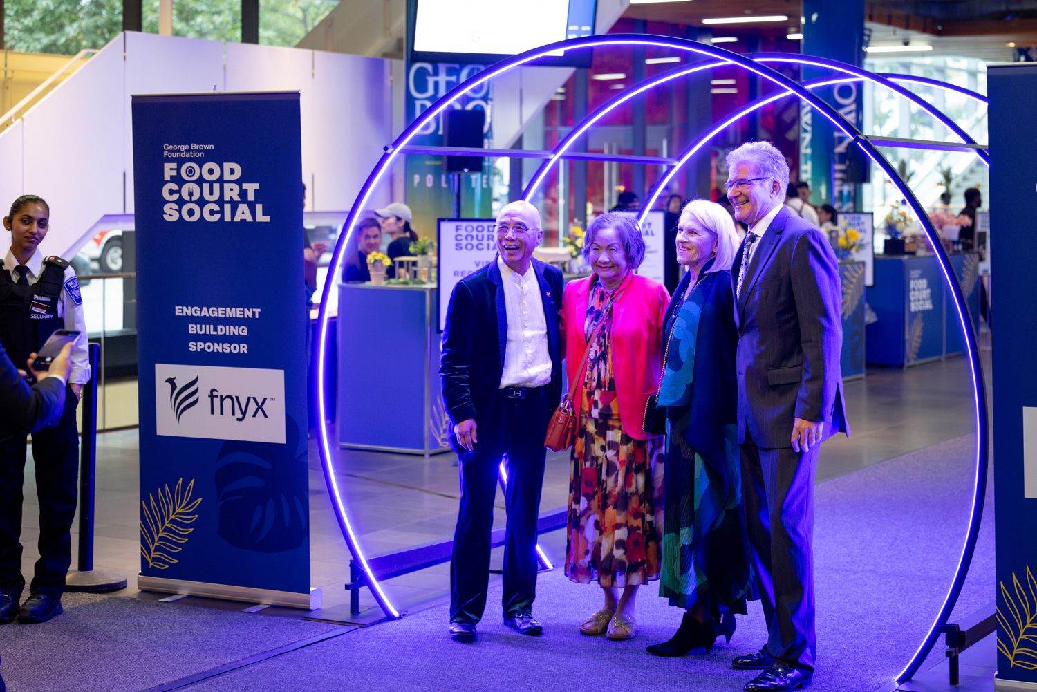Four guests at the Food Court Social stand together under a neon archway next to Food Court Social signs.