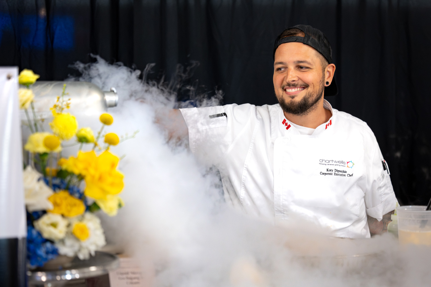 A chef uncovers a tray with steam and smoke pouring out of it.