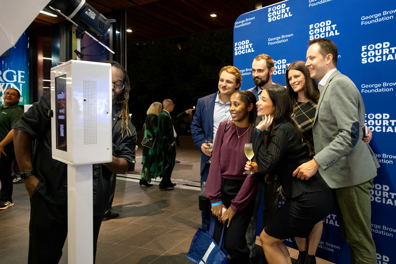 A group of guests take a photo at the selfie booth with a Food Court Social background.