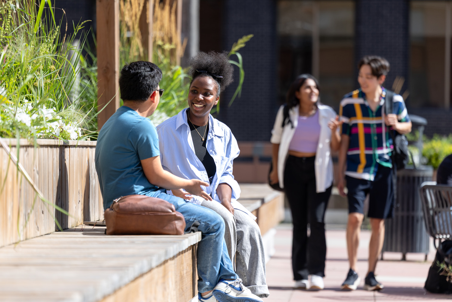 Two students are seated outside on a bench on the St. James Campus patio.