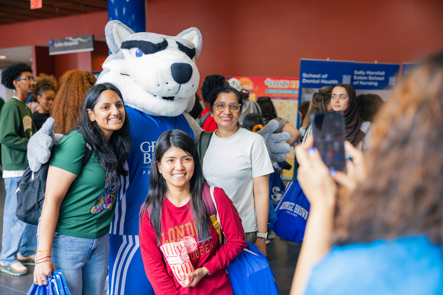 Three students pose with Helder the Husky at a Waterfront Campus event.