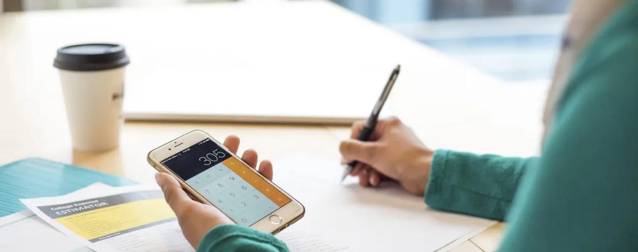 A person sitting at a table, using the calculator app on their phone.