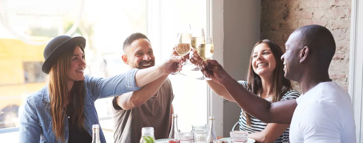 Four friends in a restaurant smiling and sharing a toast.