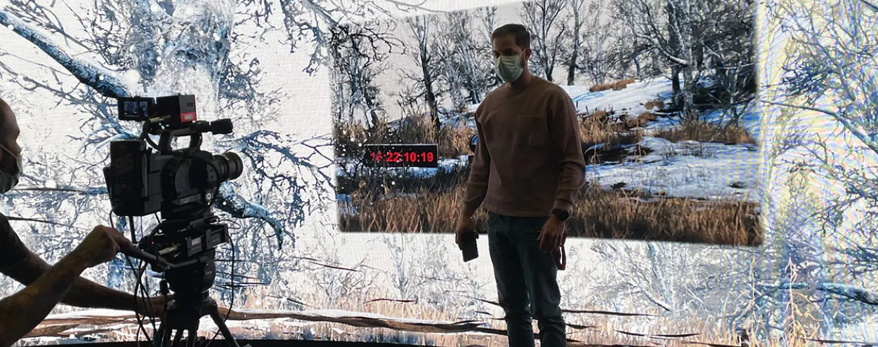 Camera and man in front of large LED screen projecting a forest