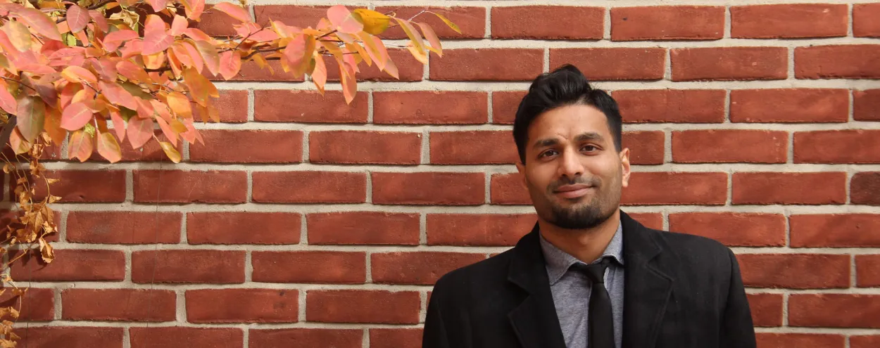 Male student posing outside of the St James patio; a brick wall is the background. 