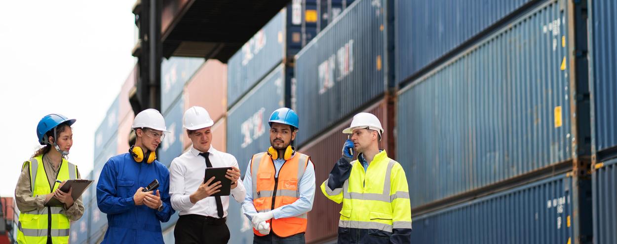 Five workers in safety gear standing in front of shipping containers