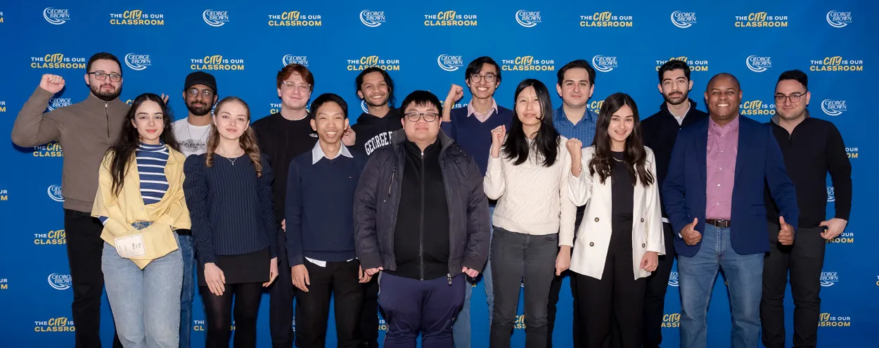 A group of computer technology students cheer in front of a GBC banner