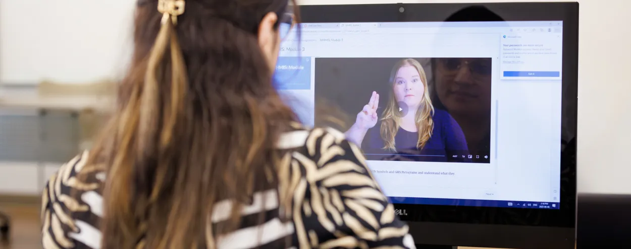 A woman looks at an American Sign Language training video on a screen