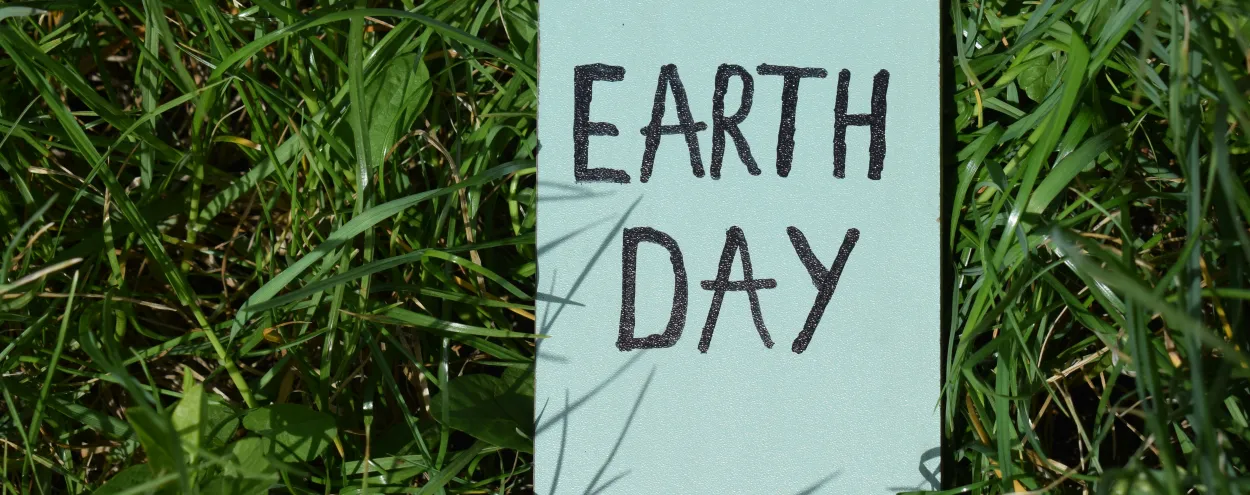 A photo of a sign that says "Earth Day" lying in the green grass.