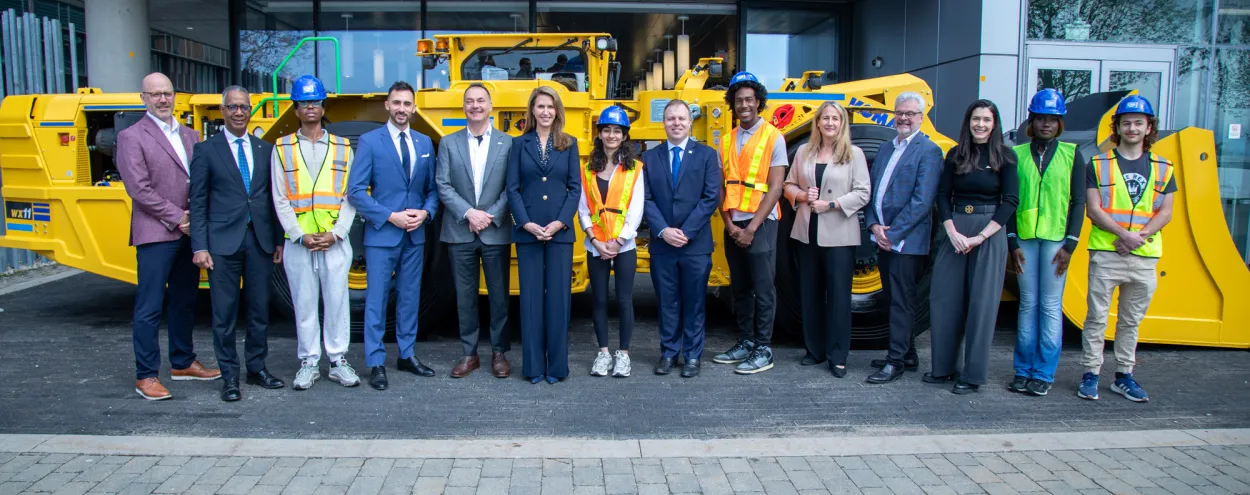 Minister Lecce, Minister Mulroney, mining leaders, students and George Brown leadership pose in a front of a mining digger at Waterfront Campus