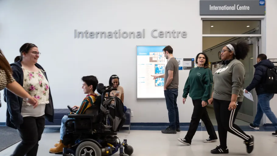 Students walking and one student driving an electric wheelchair in front of the International Centre at St. James Campus. 