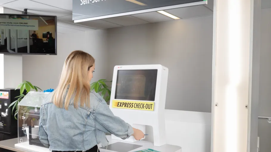 Female student using a self-serve check-out station to check-out a book at the LLC.