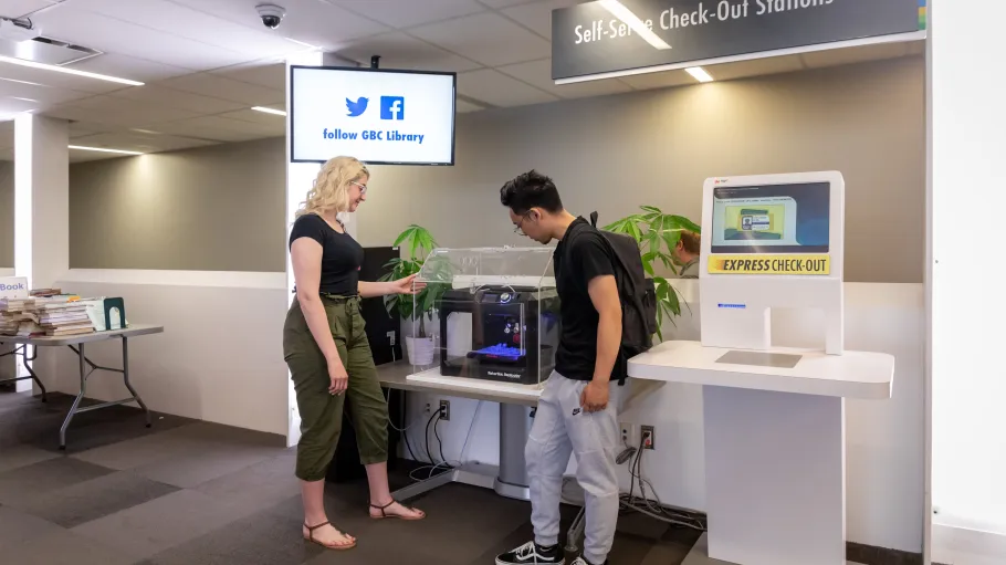 A female and male student using the 3D printer at the Waterfront Campus Library.