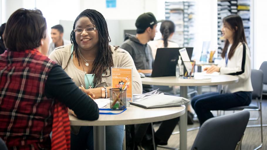 A closeup of a female student and a tutor sitting together in the Tutoring and Learning Centre. The student is listening to the tutor and smiling.