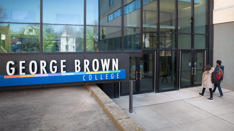 A male and female student walking towards a Casa Loma campus entrance near a George Brown Polytechnic sign.