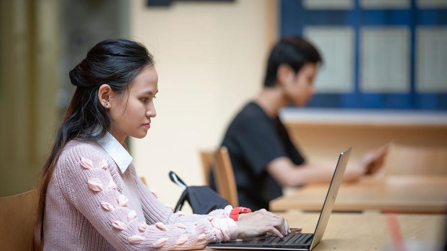 Female student using a laptop with another student in background