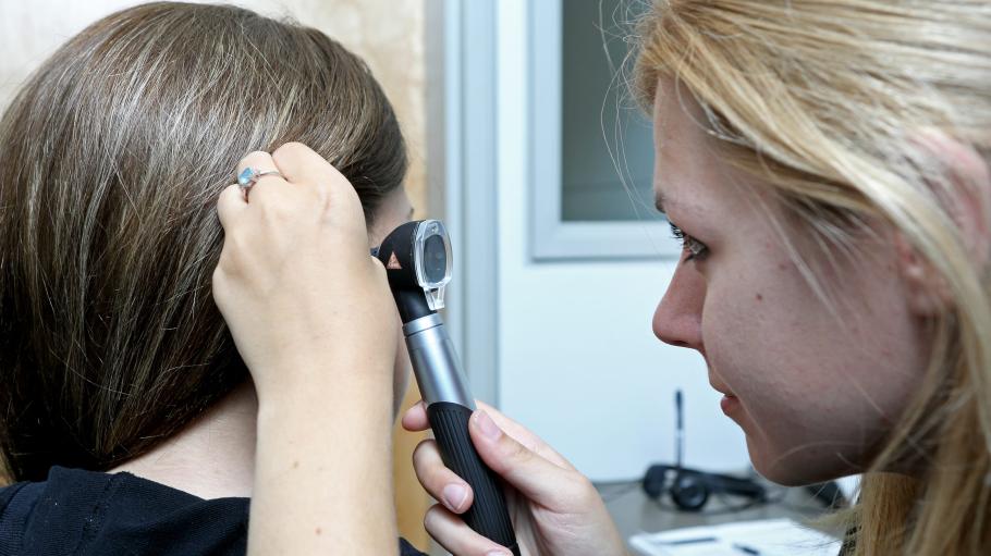 A female hearing specialist is working with a female patient where the specialist is using her equipment to observe the patient's inner ear canal.