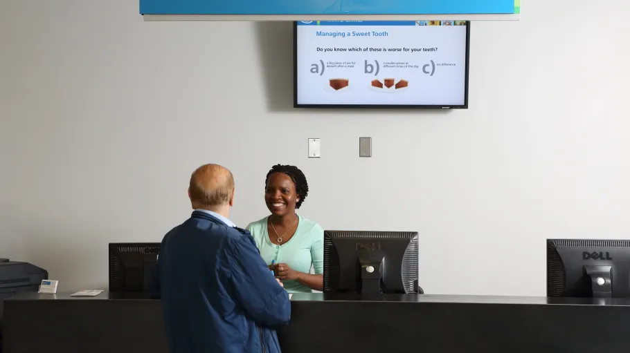 A female receptionist is behind the counter helping an elderly visitor into the office.