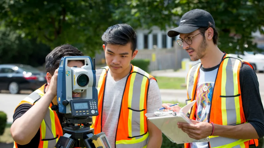 Civil engineering students working with surveying equipment outside.