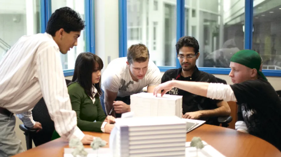 Students discuss an architectural model in a meeting room - Navigation bar - Impact Report 2019-2020