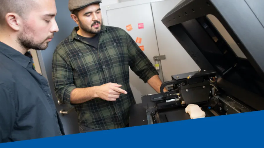 Two men stand at a 3D printer in the Maker Lab.