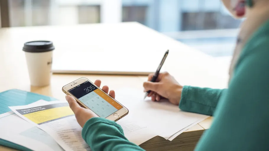 A person sitting at a table, using the calculator app on their phone.