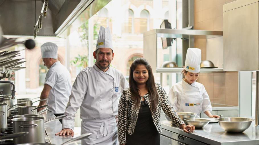 Student standing with chefs in a kitchen.