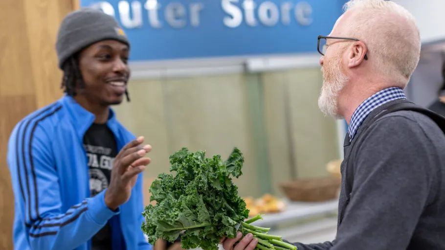 A male customer buys some kale from a Community Worker student working at the George Brown College Good Food Market, St. James Campus.