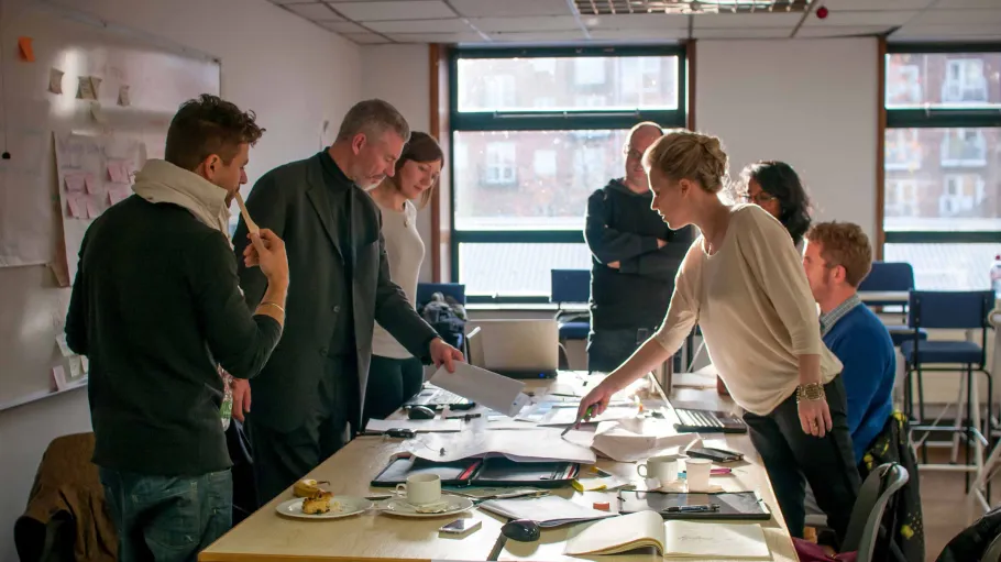 A group of people in a meeting looking at information on a table.