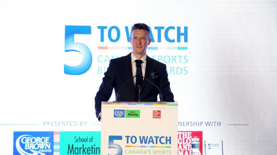 5 to Watch presenter on stage behind a podium