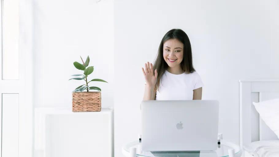 A female student in front of a computer waving to someone over an interactive call