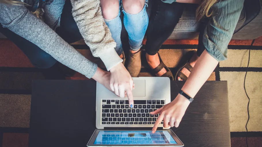 Four students gather around a laptop to work on a group project