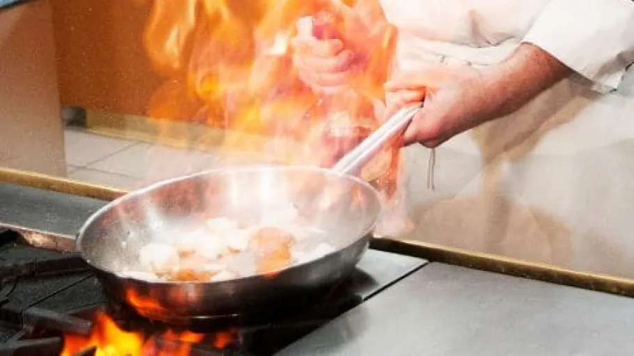 Close up of a pan flaming while cooking food.