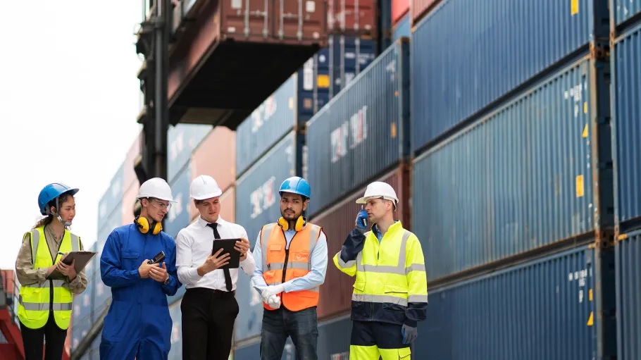 Five workers in safety gear standing in front of shipping containers