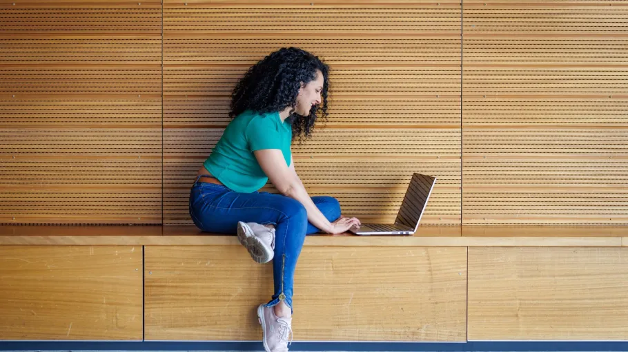 A student sits on a bench, using a laptop.