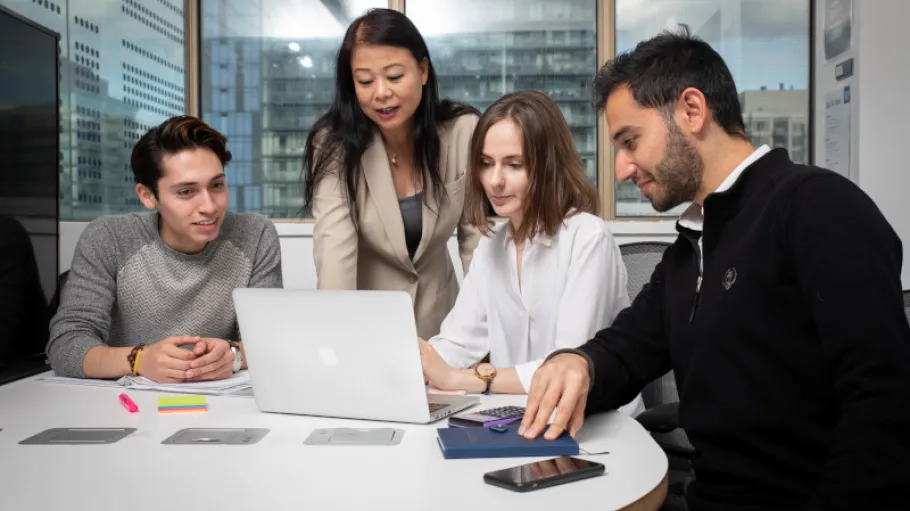 4 business students working around a laptop computer