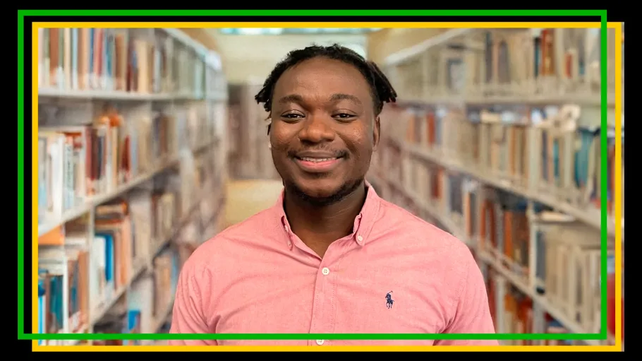 A person stands between bookshelves in a pink shirt