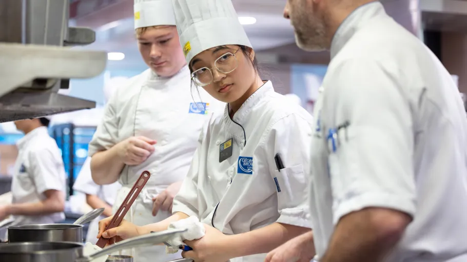 Three chefs in white clothing and chefs' hats stir