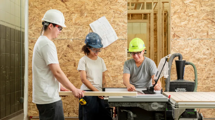 Two students and a faculty member use a table saw in the carpentry shop