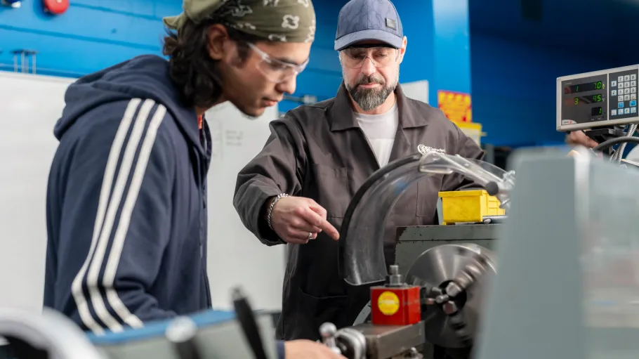 A student works on a metal lathe in the millwright lab while a faculty provides instruction
