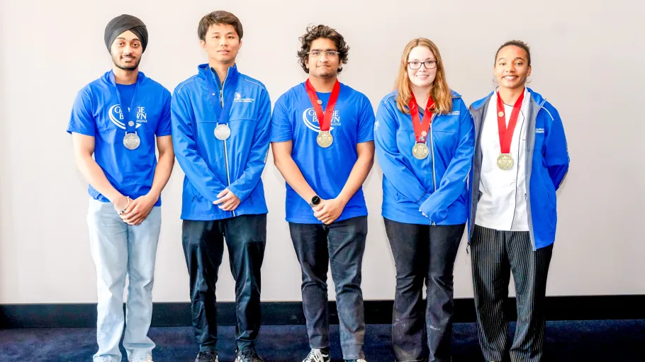 A group of five people in blue jackets wear medals around their necks