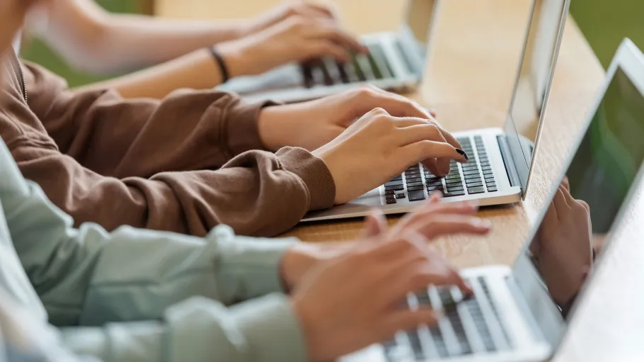 Hands from various individuals typing on individual laptops.
