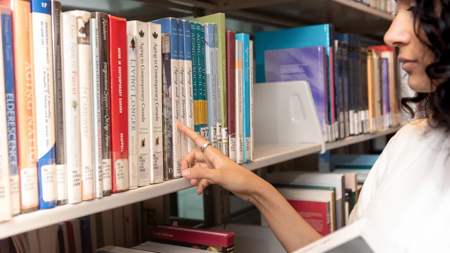 A student pointing to a book in the library book stacks.