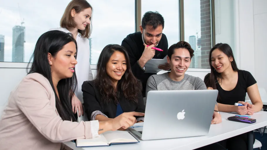 A group of students collaborate on a group assignment looking at a laptop together